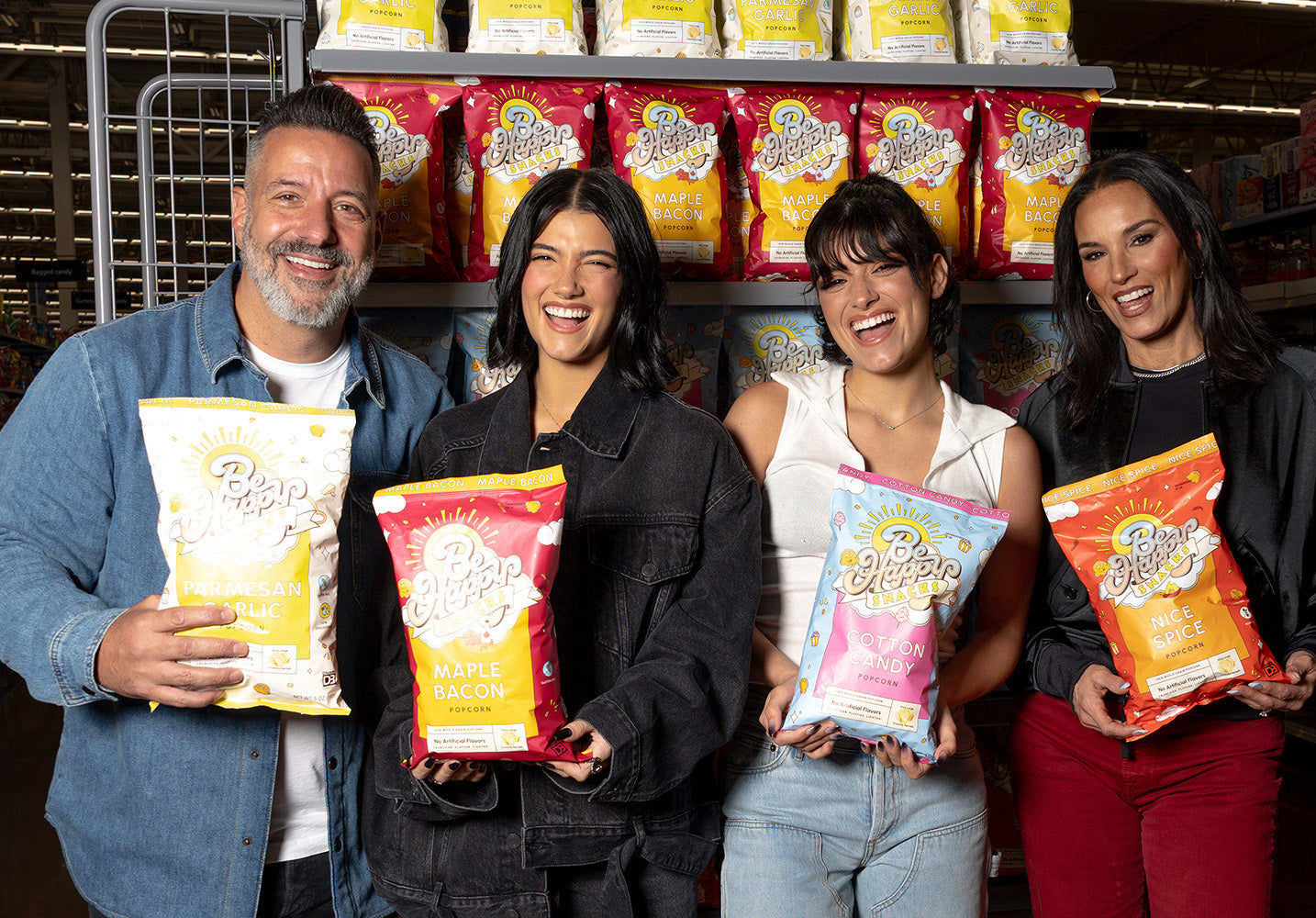 Family of 4 standing in a shopping store holding up bags of Be Happy Snacks Popcorn